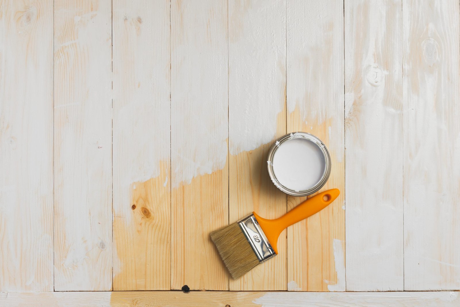 Paintbrush and can on a partially painted wood surface